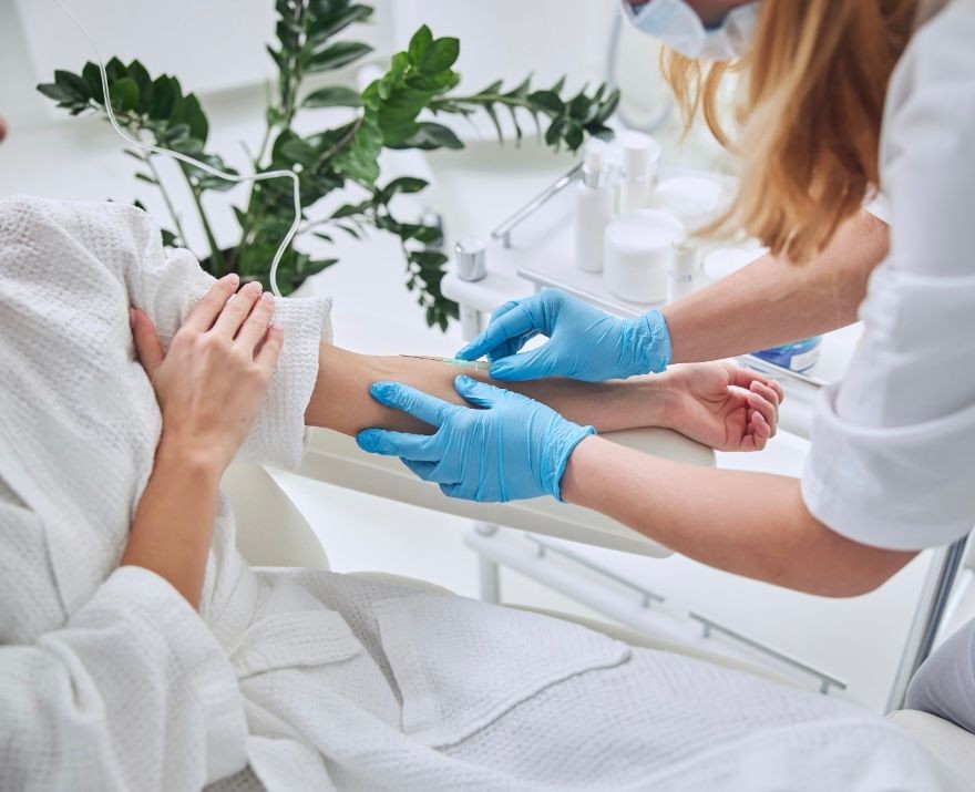 Medical professional wearing gloves inserting an IV into a patient's arm in a clinical setting.