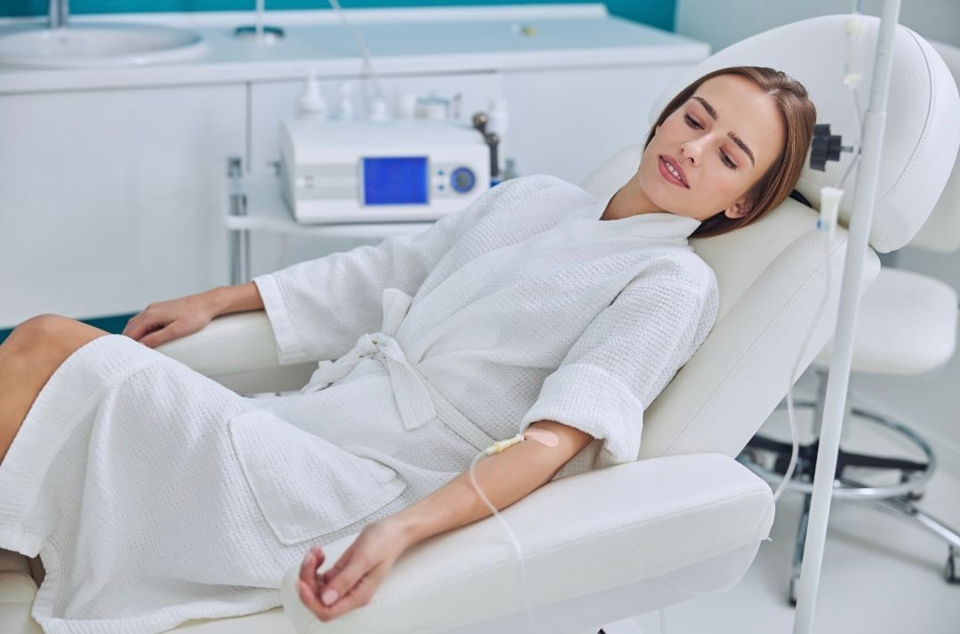 Woman in a spa robe receiving IV therapy while reclining in a medical spa chair.